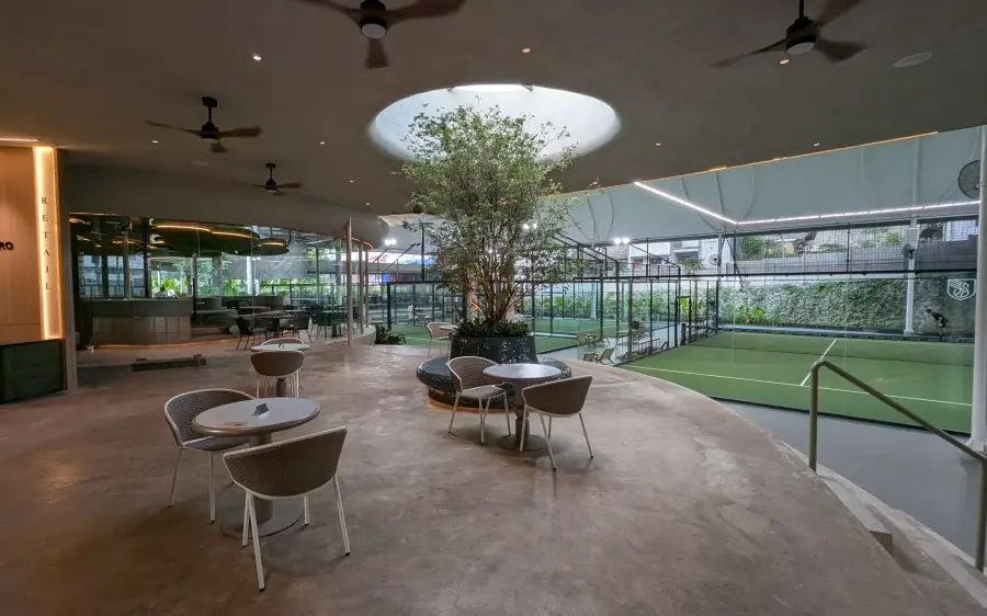 Café tables around a tree under a skylight, courts beyond