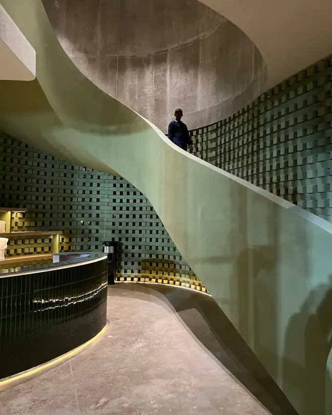 Sculptural spiral staircase beside the green-tiled bar